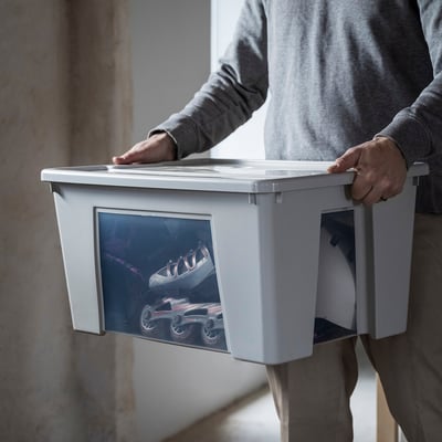 A person holding a light grey SAMLA storage box with clear sides, filled with roller skates, emphasising its size and visibility.