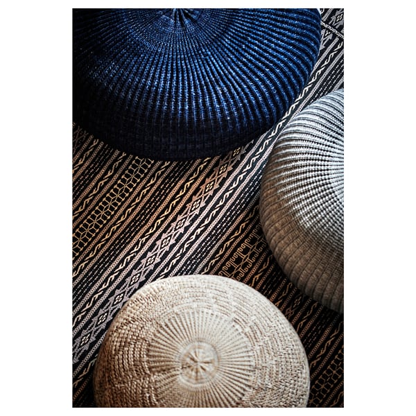 Three colorful knitted poufs in blue, beige, and grey with intricate patterns are stacked together.