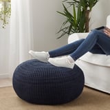 Person rests feet on round navy blue footstool, seated in white chair with tablet, near green plant.