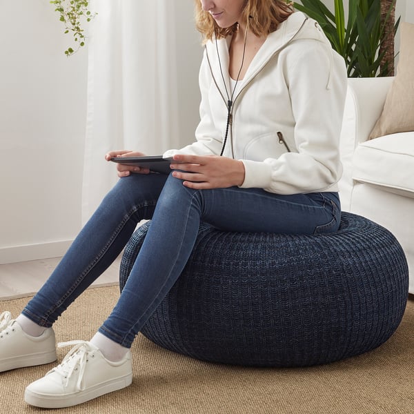 Person sitting on blue pouffe, using tablet and wearing white hoodie, jeans, and sneakers.