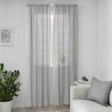 Grey checkered curtains hang by window, partially covering plant and chair, creating cozy atmosphere.