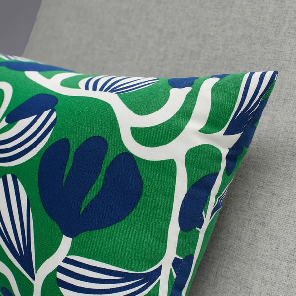 Bright, colorful cushion with large green and blue leaf patterns, resting on a gray surface. High-quality fabric and intricate design.