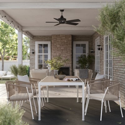 Outdoor patio with modern white dining set, black ceiling fan, brick wall, and greenery.