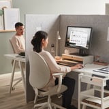 Office with gray room dividers and desks, each with computers and personal items.