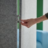 Hand adjusting metal clasp on gray room divider, connecting two panels at a corner.