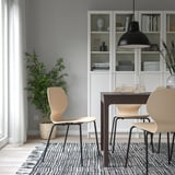 Modern dining set with light wood chairs, dark table, black pendant light, green plant, and white bookshelf with decor.