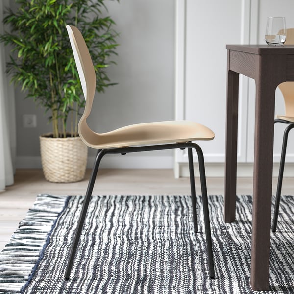 Modern chair with bent backrest, light wood seat, dark metal legs, set near wooden table with glass and potted plant.