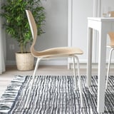Modern chair with curved back for support, on striped rug near plant and table.