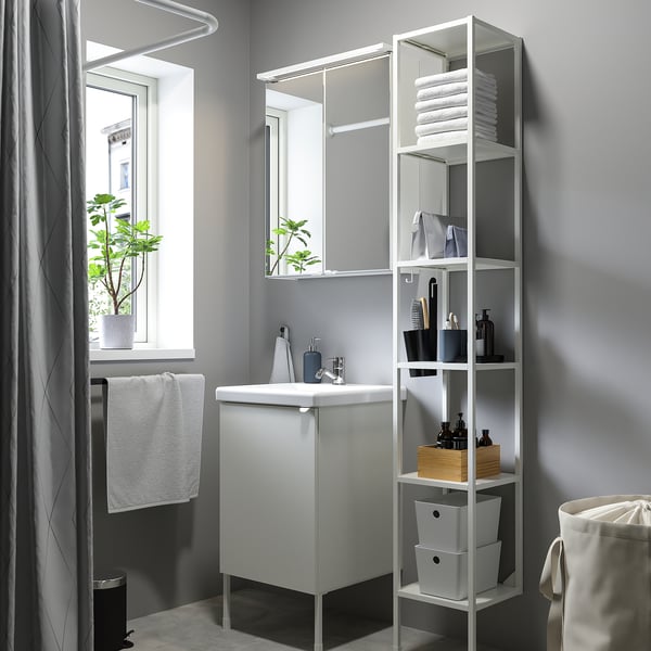 Modern bathroom: white cabinet, mirror with lights, tall shelving with towels, window with plant, gray walls, shower curtain.