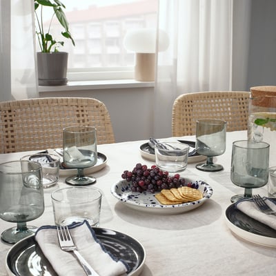 Table set with SILVERSIDA glassware and plates. Plates hold grapes and crackers. Wicker chairs surround the table.