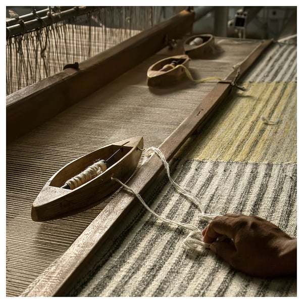 Handcrafted grey and yellow wool rug on loom, showing intricate weaving process.