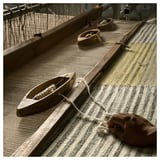 Handcrafted grey and yellow wool rug on loom, showing intricate weaving process.