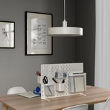 SKÅDIS white desk divider with pockets on wooden desk. Pens, scissors, notebook. Two wall art pieces. Central light.