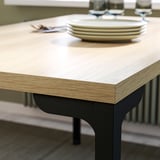 Modern wooden table with dark metal legs. Neatly set with plates and glasses.