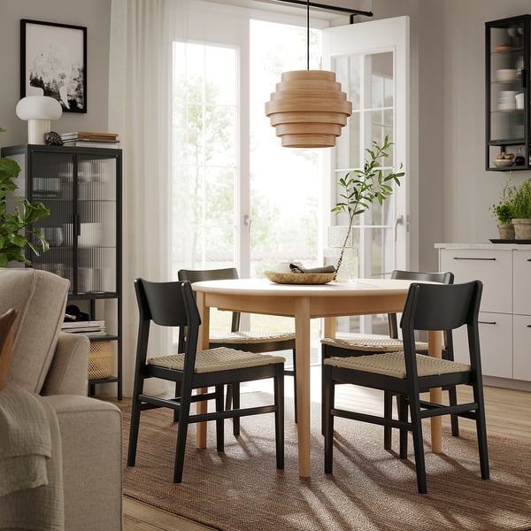 Modern dining area with SKANSNÄS light wood table surrounding by black chairs, unique pendant light, large window.