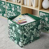 Storage bin with green, nature-themed design holds childrens drawing paper and crayons.
