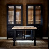 Modern black coffee table with wooden top, flanked by matching black cabinets with glass doors. Cozy, stylish room setting.