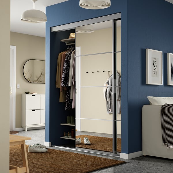 Modern room with SKYTTA mirrored closet, blue walls, white furniture, and wooden accents; closets large mirror reflects room.
