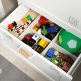 White toy chest with divided drawers holding various colorful toys.