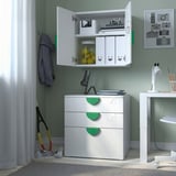 White storage unit with open cabinet displaying toys and books. Green handles and hooks featuring nearby desk and sports gear.