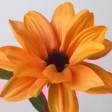Orange artificial daisy with green leaves, recycled, vibrant petals and black center, plain background.