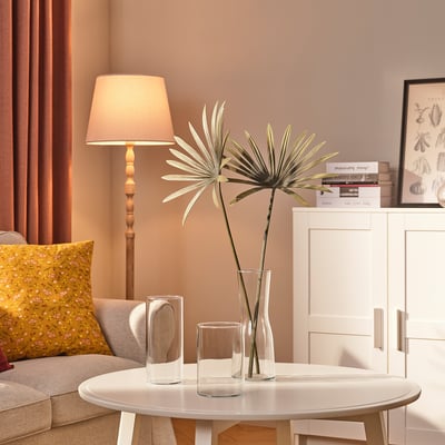 Modern living room with cream sofa, yellow pillow, coffee table, vases, bookshelf, lamp, red curtains.