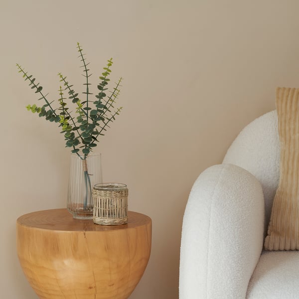 A cozy corner with a white boucle chair, wooden stool, and artificial eucalyptus plant.