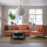 Modern living room with SÖDERHAMN sofa in coral, pendant light, coffee table, plant, lamp, art, and large windows.