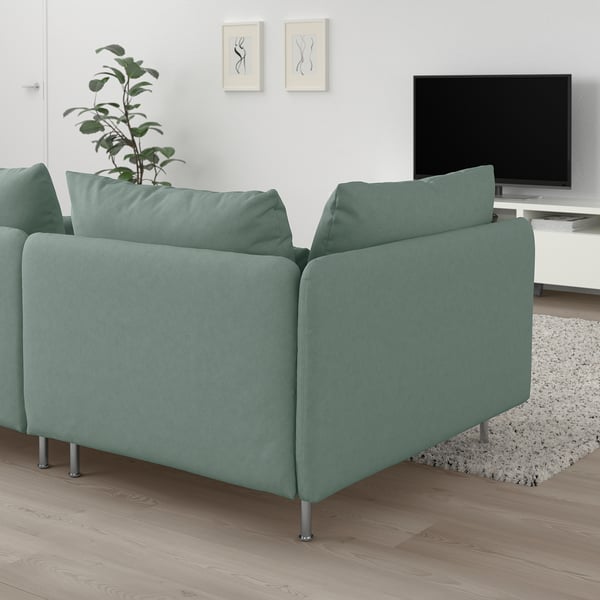 Corner of a sage green SÖDERHAMN sofa with metal legs and cushions, beside a tv and plant.