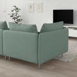 Corner of a sage green SÖDERHAMN sofa with metal legs and cushions, beside a tv and plant.