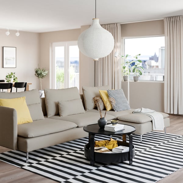 Modern living room with beige SÖDERHAMN sofa, yellow pillows, black & white rug, round coffee table, large windows, and white pendant lamp.