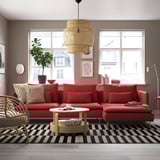 Red SÖDERHAMN sofa in cozy living room with large window, plush cushions, wooden floors, black/white rug, rustic coffee table, and pendant light.