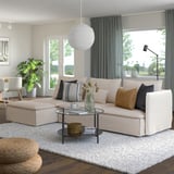 Modern beige SÖDERHAMN sectional sofa with cushions, glass coffee table, large window, and plants in bright living room.