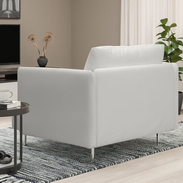 Modern minimalist living room: large white SÖDERHAMN armchair on rug, beside small table with cup, books, and vase, near tv and plant.