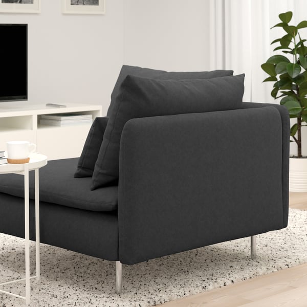 Dark gray modern sofa with three cushions, positioned in a cozy room with a white side table holding a coffee cup.