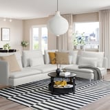 Minimalist living room with white SÖDERHAMN sectional, black coffee table, striped rug, and large window with city view. Cozy and modern design.