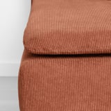 Close-up of a well-cushioned, textured footstool in rust-colored corduroy.