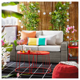 Bright outdoor sectional sofa with colorful pillows, red side tables, and lush plants.