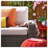 Cozy outdoor seating with orange and gray cushions on a dark wicker sofa.