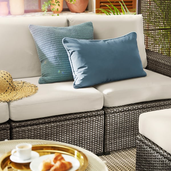 Modern outdoor wicker sofa with beige cushions and blue pillows, featuring a woven design and natural decorations.