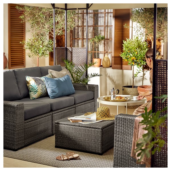 Modern outdoor living area with grey SOLLERÖN modular sofa, colorful pillows, round table, and potted plants.