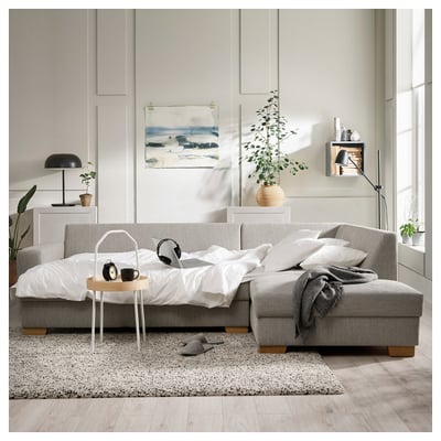 Modern, grey SÖRVALLEN sofa, minimalist design with white pillows, black lamp, wooden table, and cozy bedding setup.