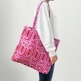 Person carrying a red patterned reusable tote bag over shoulder.