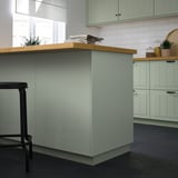Modern kitchen with green panel, butcher block counter, stool & plant.