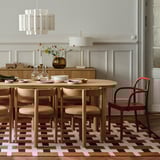 Modern dining room with oval wood table, six chairs, colorful rug, and pendant lamp.
