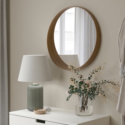 Circular mirror on wall, desk with green lamp and vase.