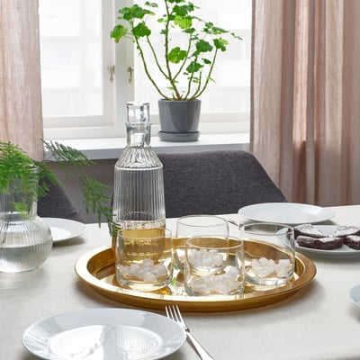 Table setting with STORSINT glassware and carafe on a gold tray, surrounded by plates and utensils.