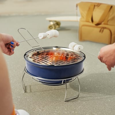 Two people roasting marshmallows on a blue, portable STRANDÖN grill with carrying handle.