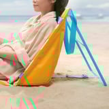 A person relaxes on a yellow STRANDÖN beach chair. The chair has blue straps and a storage bag at the back, perfect for a day at the beach.