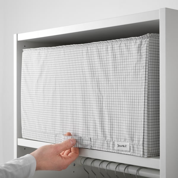 Person placing grid fabric storage box labeled towels into white shelf.